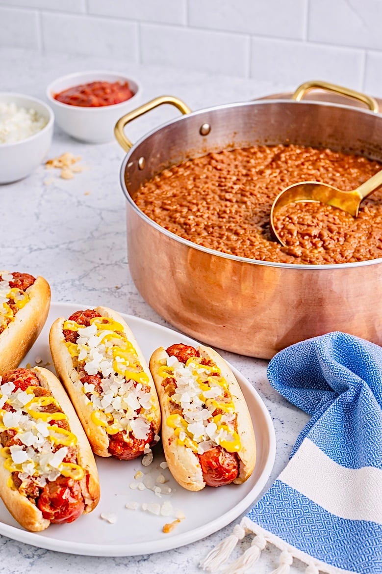 Coney Island hot dogs with chili sauce yellow mustard and diced onions beside a pot of chili