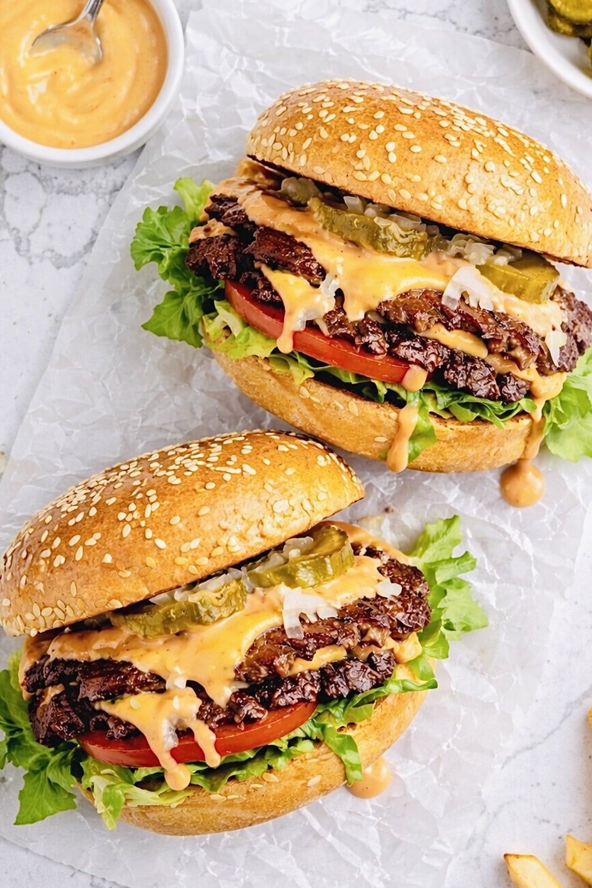 Two homemade smash burgers with crispy beef patties, melted cheddar, pickles, lettuce, tomato, onion, and burger sauce