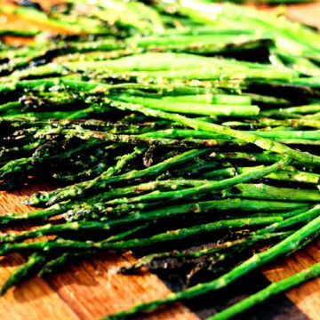 Easy grilled asparagus with garlic, olive oil, and light char marks on a wooden board.