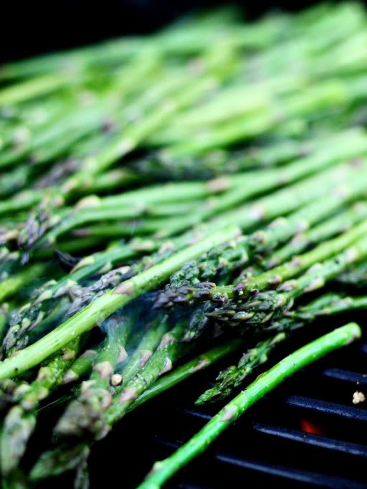 Asparagus arranged on hot grill grates for grilling.