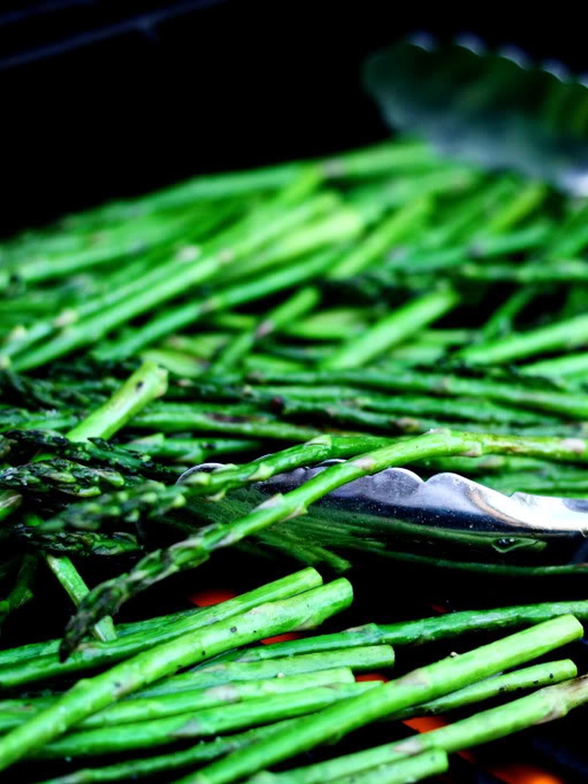 Tongs turning grilled asparagus spears over hot grill grates.