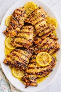 Juicy grilled lemon chicken breasts on a white platter with lemon slices and parsley