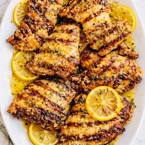 Juicy grilled lemon chicken breasts on a white platter with lemon slices and parsley