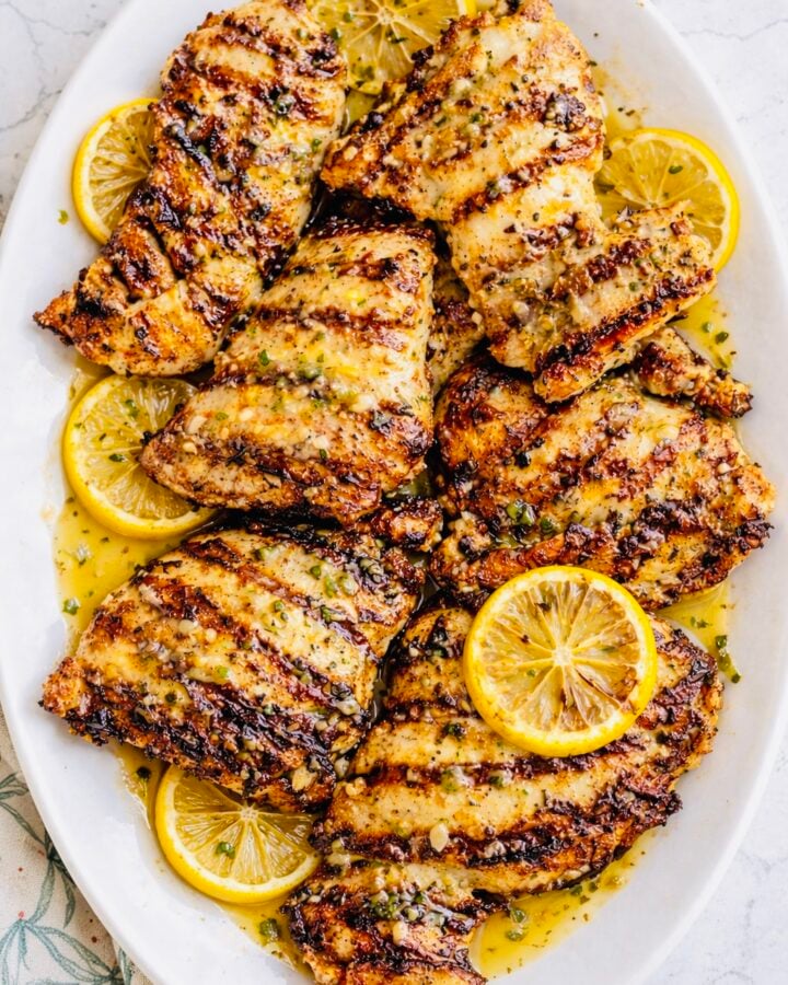 Juicy grilled lemon chicken breasts on a white platter with lemon slices and parsley