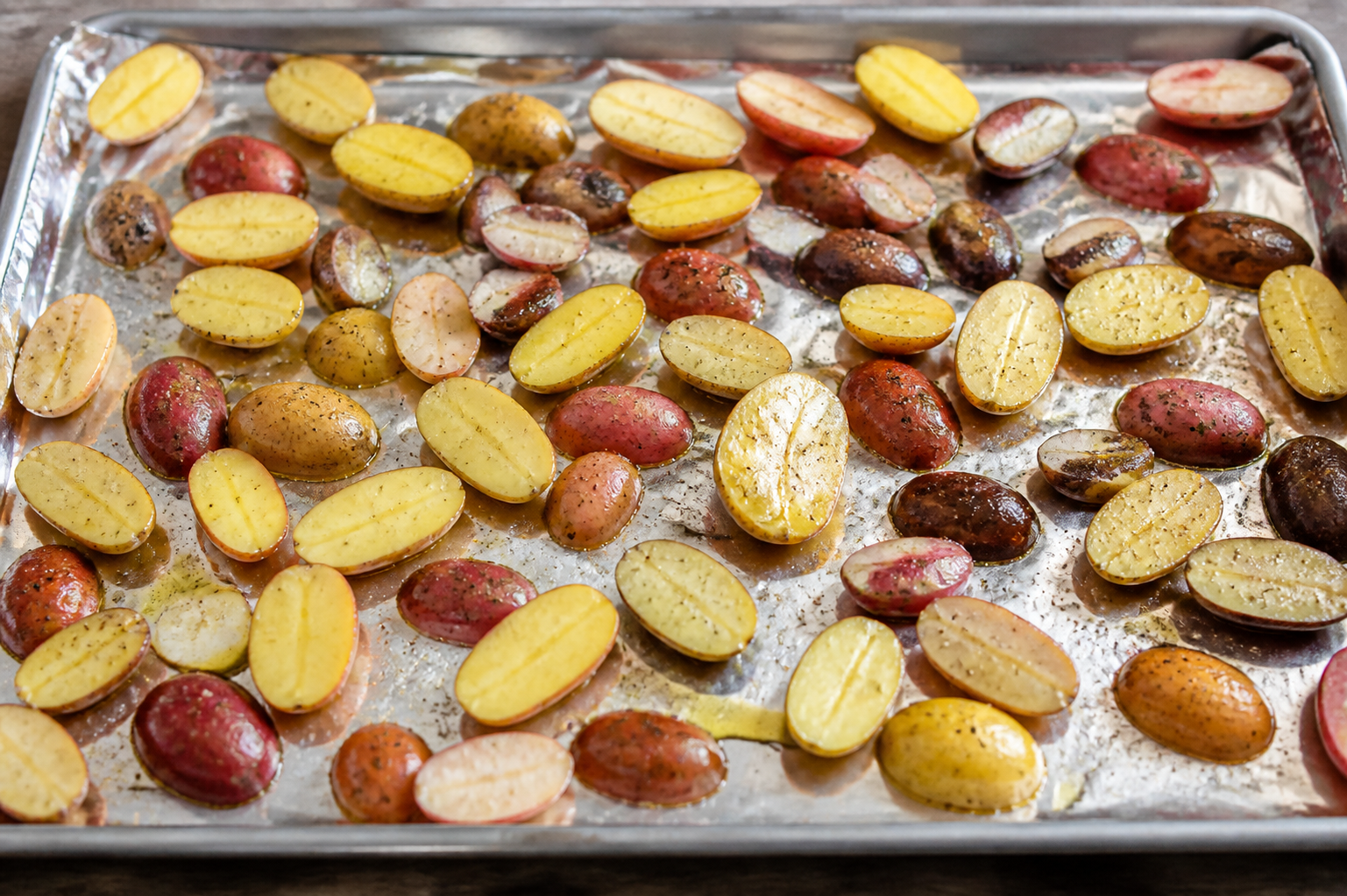 Seasoned fingerling potatoes spread in a single layer on a foil-lined sheet pan before roasting