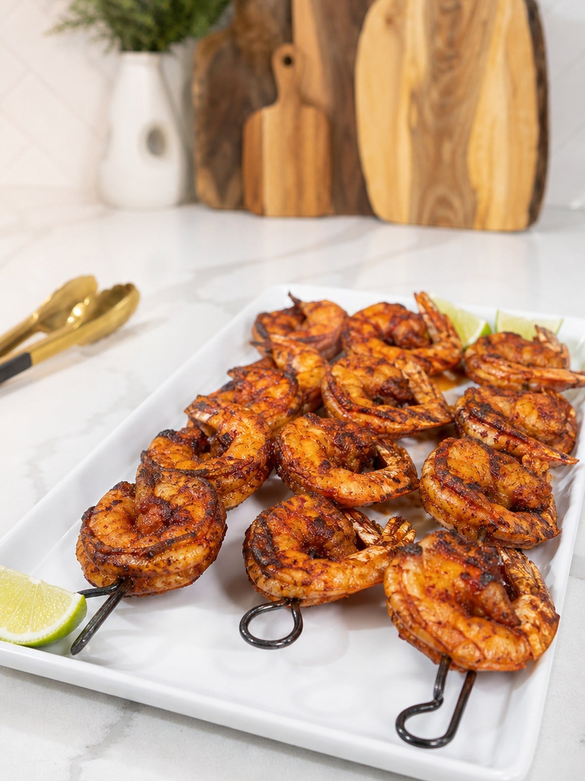 Finished BBQ grilled shrimp skewers on a white platter with lightly charred orange-red seasoning.