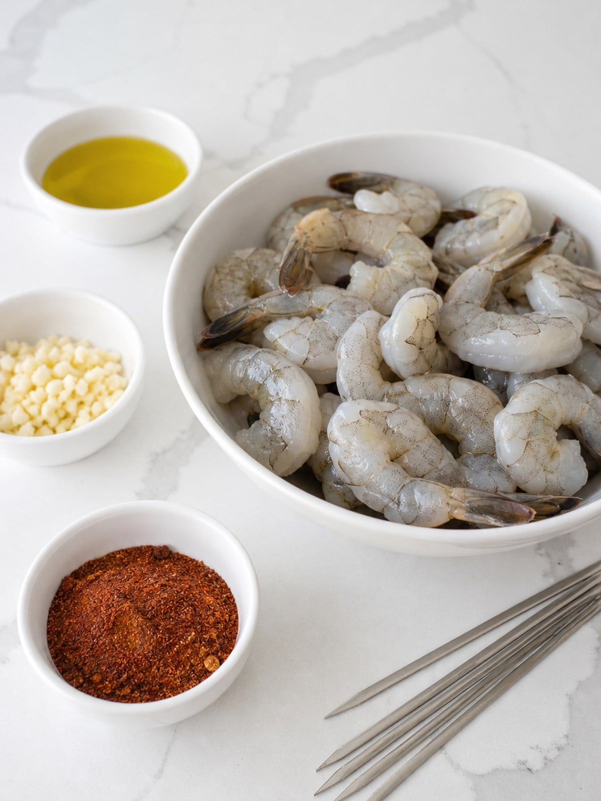 Raw deveined shrimp with olive oil, garlic, chipotle spice rub, and metal skewers for BBQ grilled shrimp skewers.