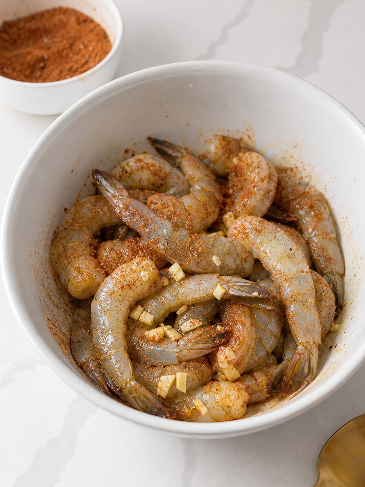 Raw shrimp tossed with olive oil, garlic, and chipotle brown sugar spice rub in a white bowl.