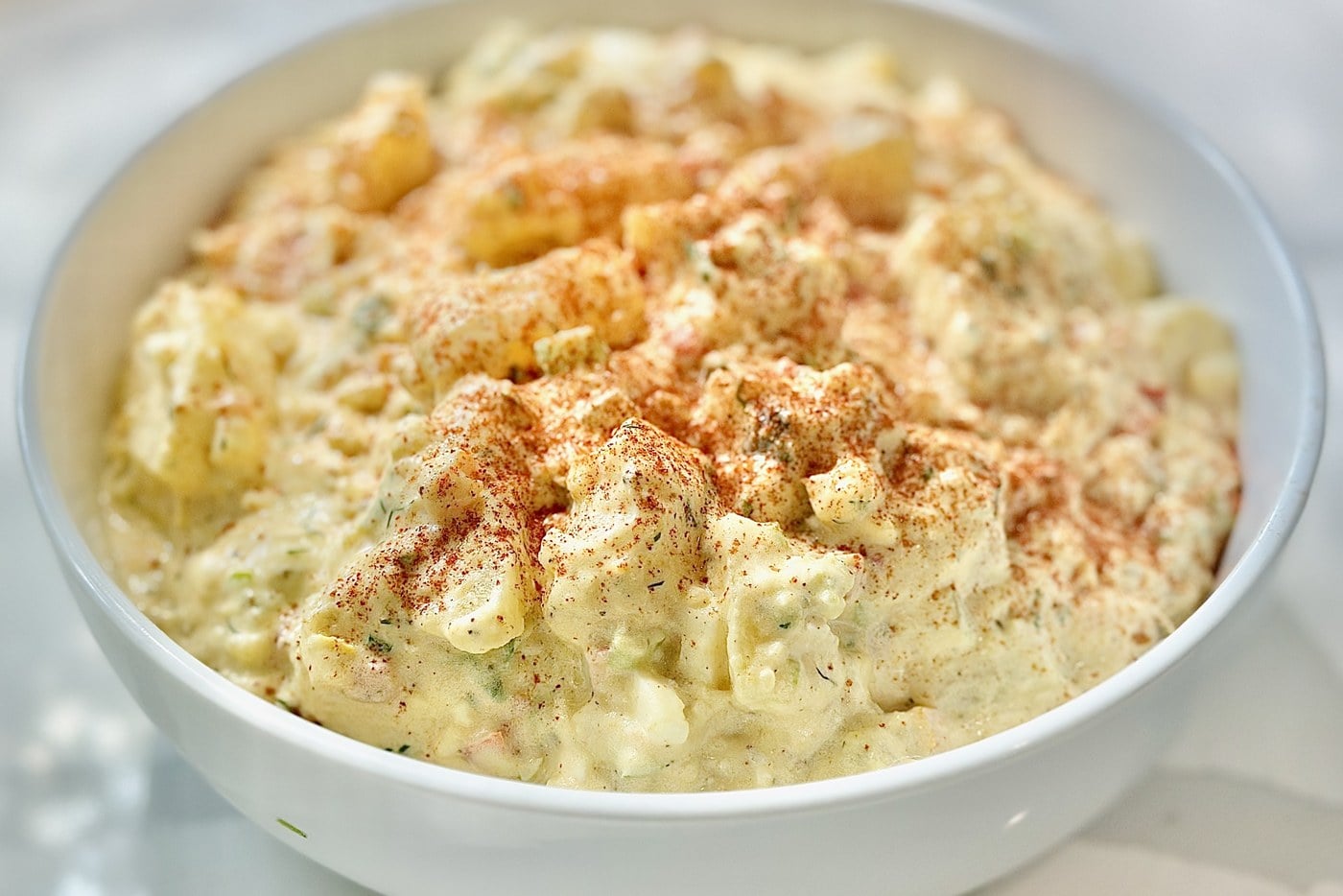 Bowl of creamy Southern potato salad topped with paprika and fresh dill.