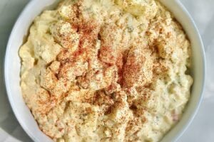 Creamy Southern potato salad with Yukon Gold potatoes, chopped eggs, dill pickles, fresh dill, and paprika in a white bowl.
