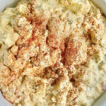 Creamy Southern potato salad with Yukon Gold potatoes, chopped eggs, dill pickles, fresh dill, and paprika in a white bowl.