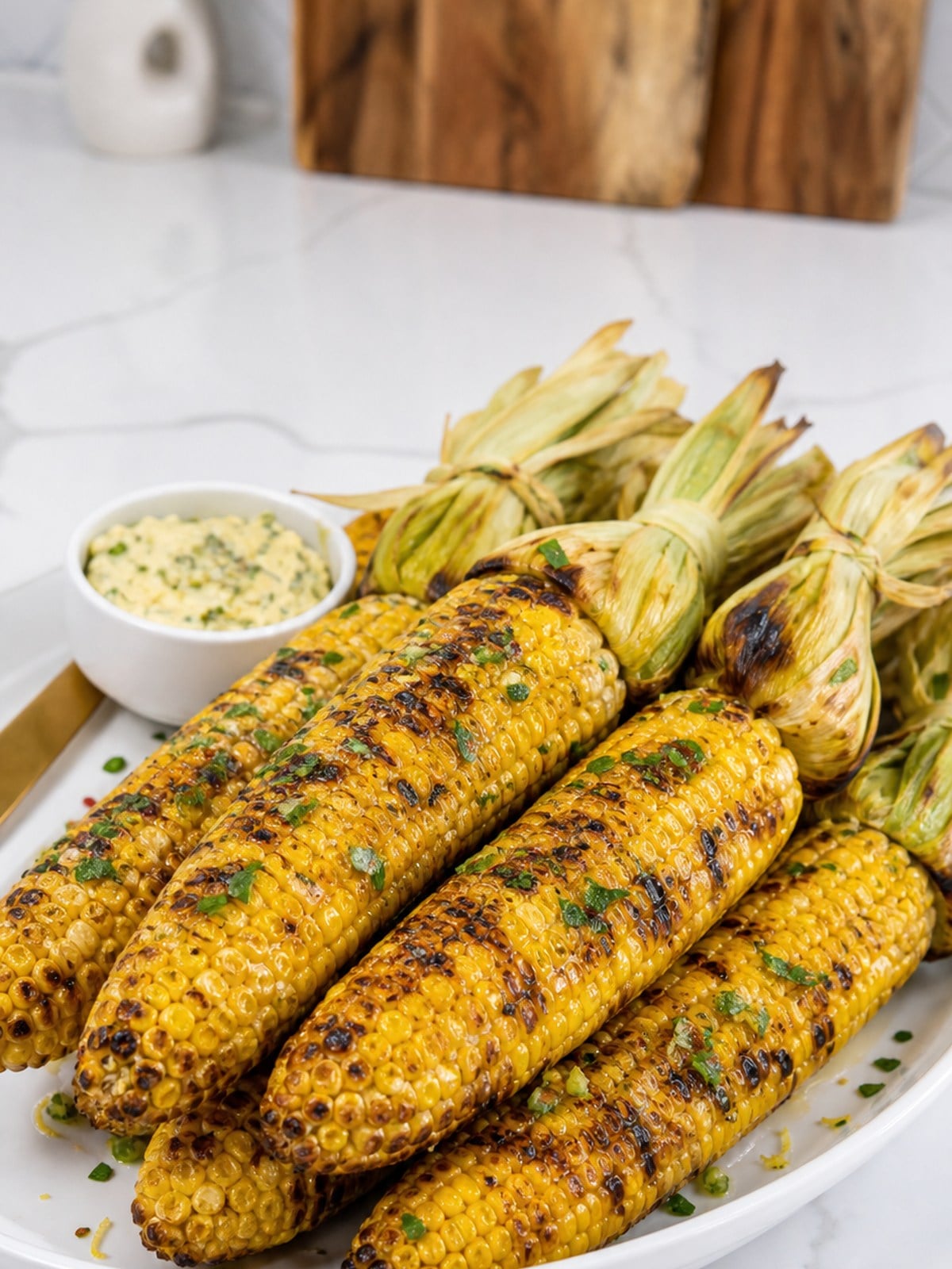 Finished grilled corn on the cob with garlic herb butter on a white platter.