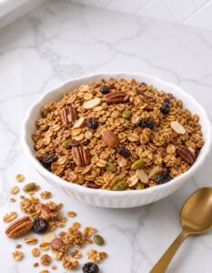 Finished homemade granola in a white bowl with toasted oats, nuts, seeds, and optional dried fruit.