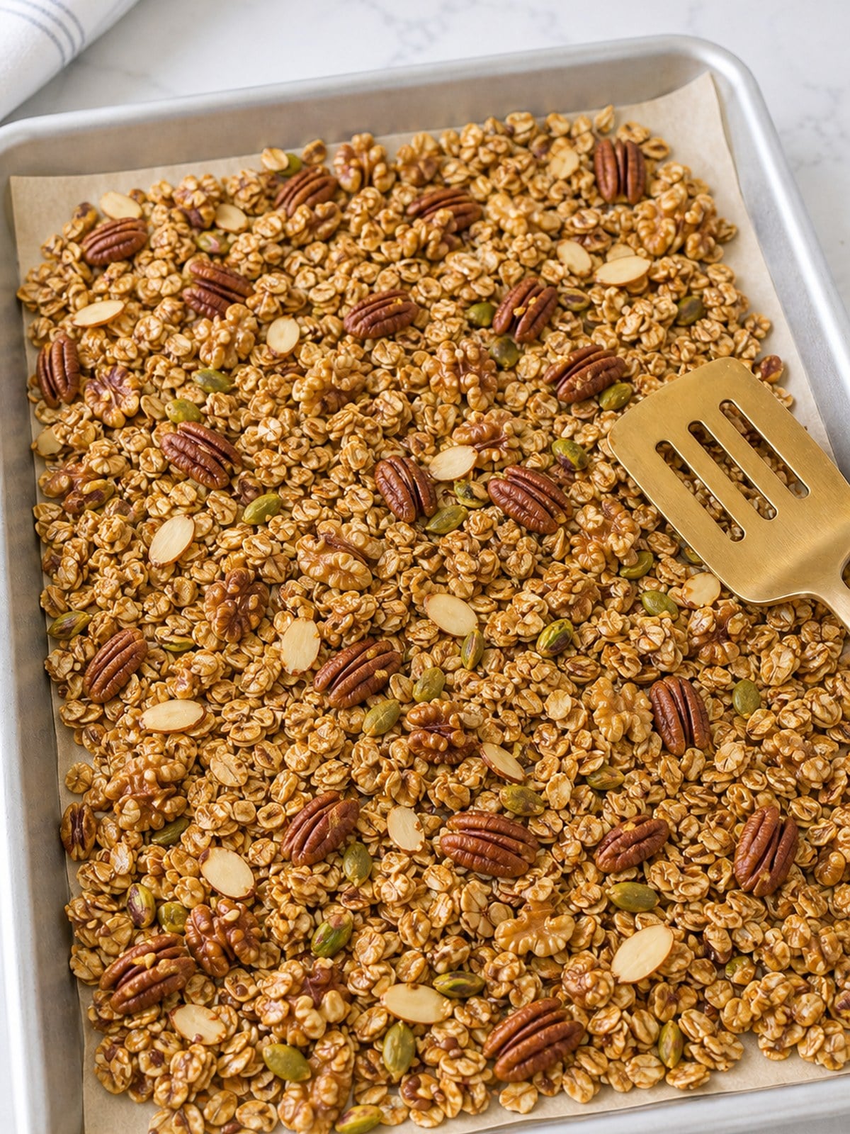 Granola mixture with oats, nuts, and seeds spread on a parchment-lined baking sheet.
