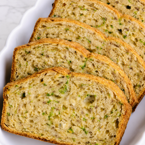 Close view of tender zucchini bread slices showing green zucchini flecks and golden crust.