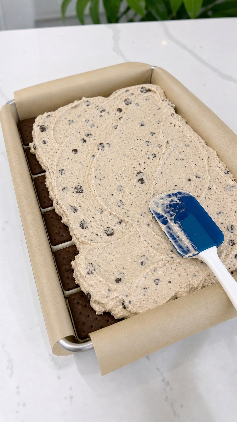 Smooth cookie ice cream spread over vanilla ice cream sandwiches in a parchment-lined pan.