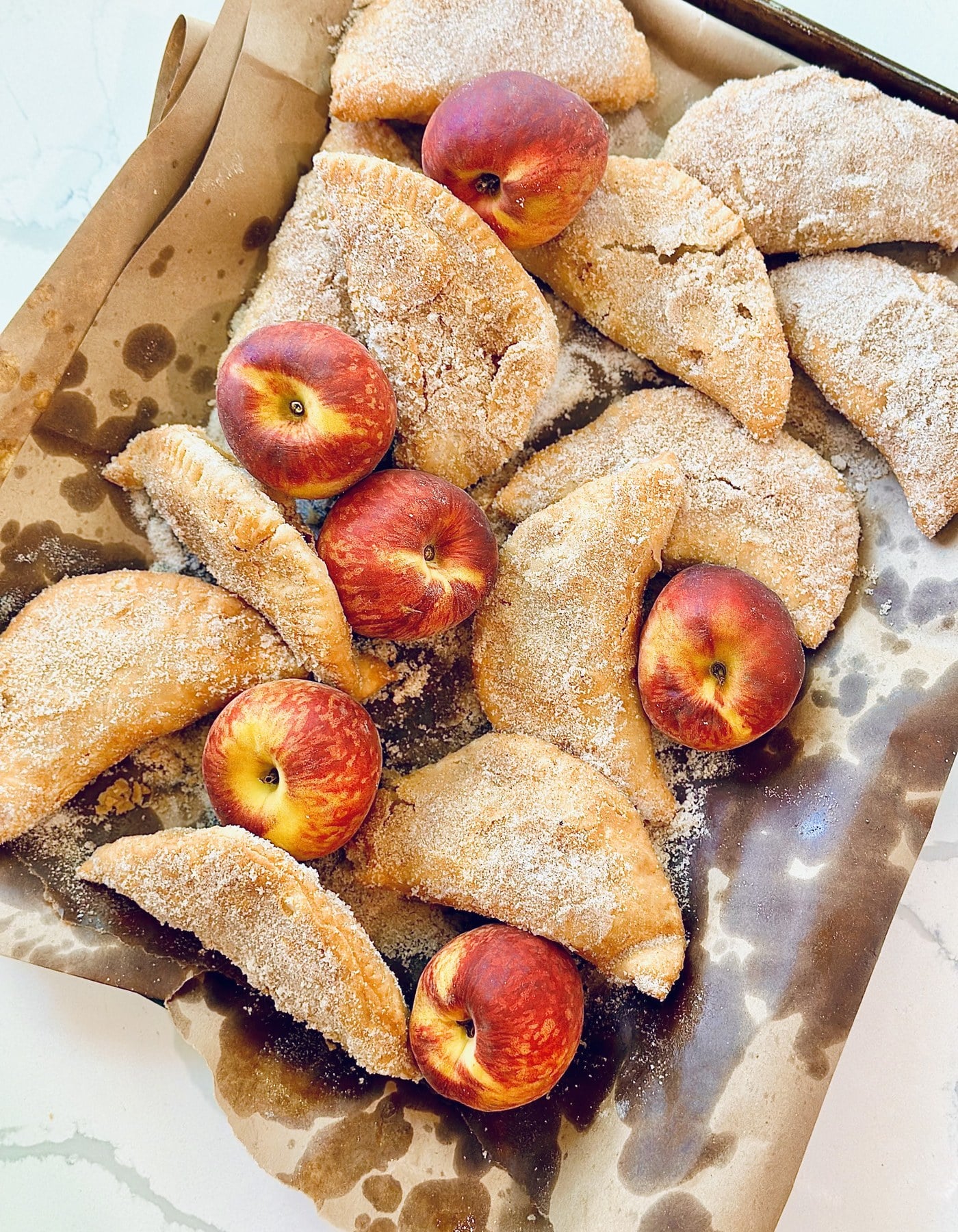 Southern fried peach pies coated in cinnamon sugar with fresh peaches on parchment.