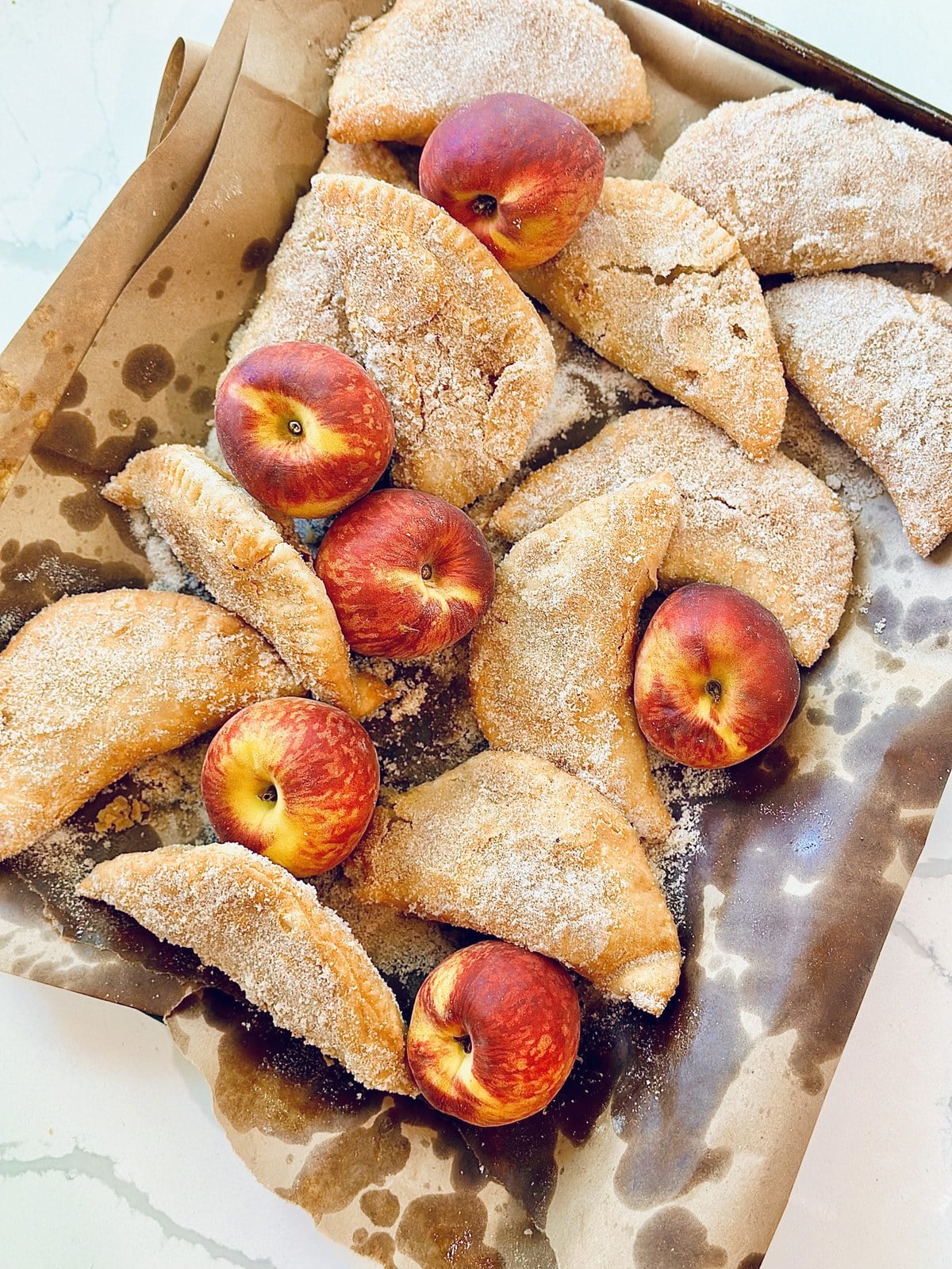 Finished peach fried pies showing cinnamon sugar crust and fresh peaches.