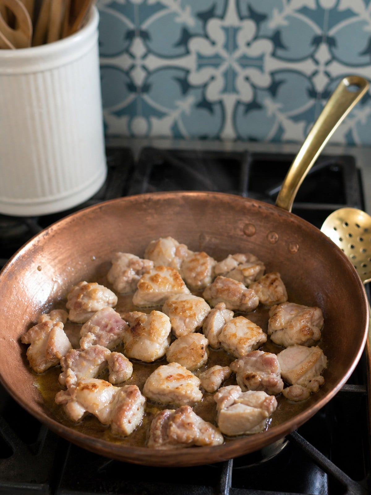 Chicken thigh pieces browning in a copper skillet for slow cooker Massaman curry.