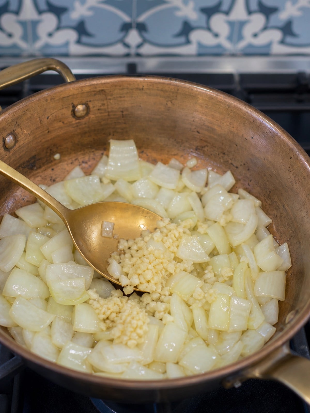Onions and minced garlic cooking in a copper skillet for Massaman chicken curry.