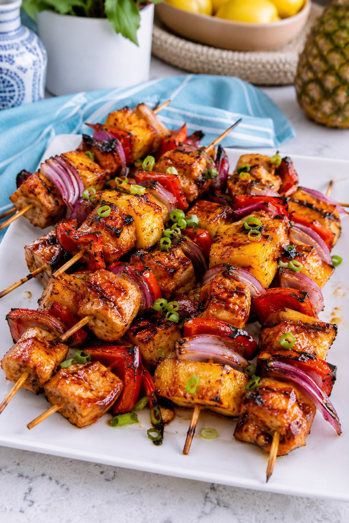 Close view of grilled Hawaiian chicken skewers with pineapple, peppers, onion, and green onion garnish.