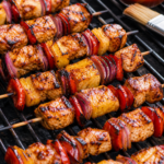 Hawaiian chicken skewers grilling with pineapple, red bell pepper, red onion, charred edges, and glossy reserved marinade.