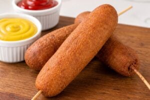 Homemade state fair corn dogs with yellow mustard and ketchup on a wooden board.