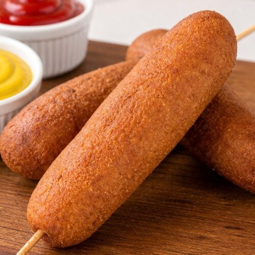 Homemade state fair corn dogs with yellow mustard and ketchup on a wooden board.