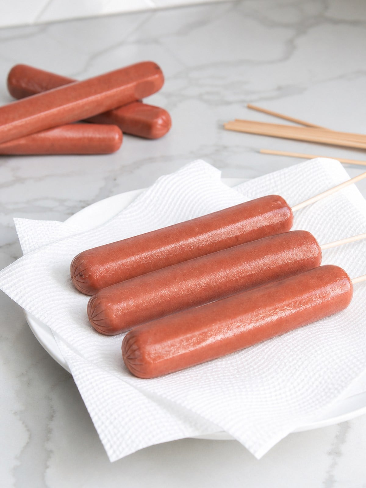 Skewered hot dogs drying on paper towels before dipping in corn dog batter.