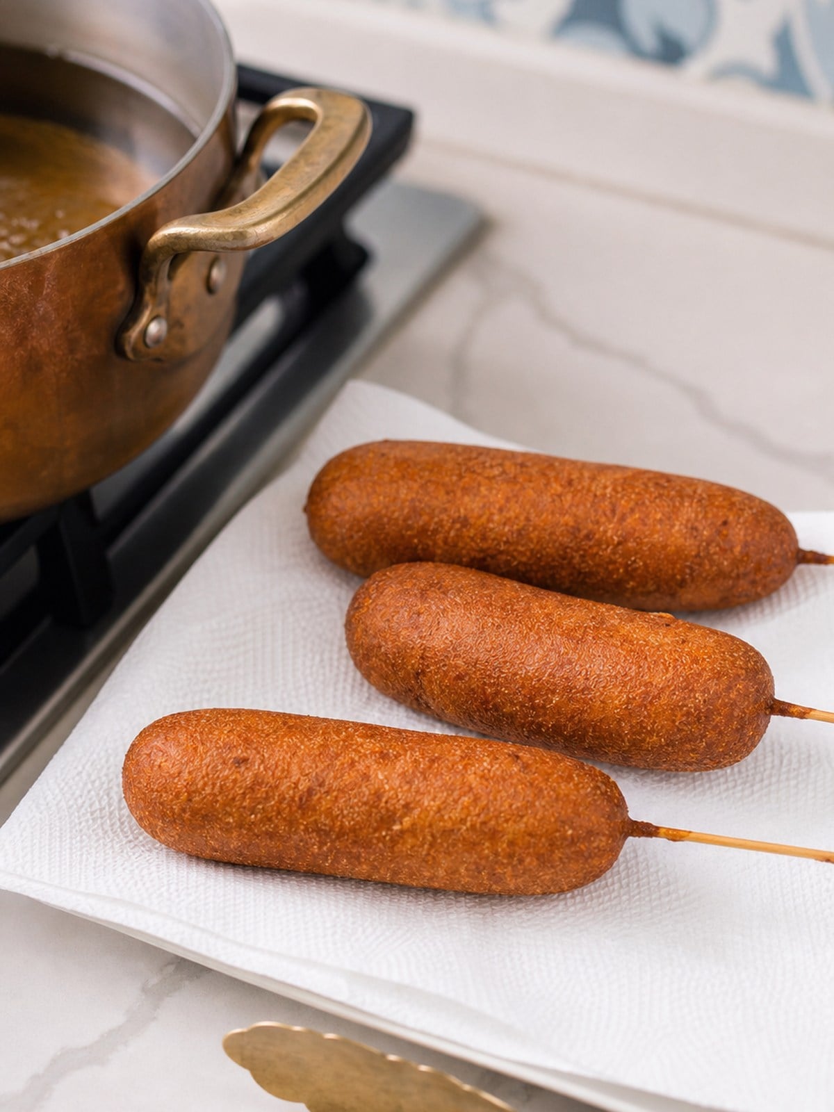 Freshly fried corn dogs draining on paper towels after cooking until golden brown.