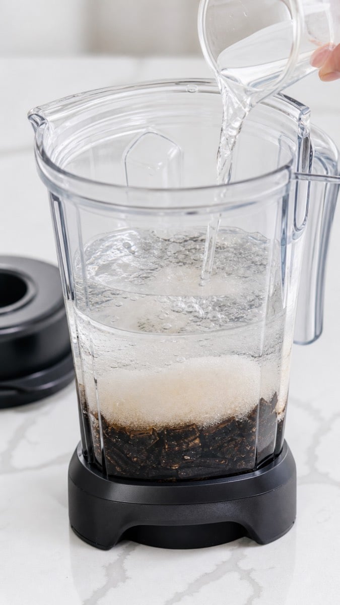 Chopped vanilla beans, sugar, water, vodka, and corn syrup layered in a blender before blending.