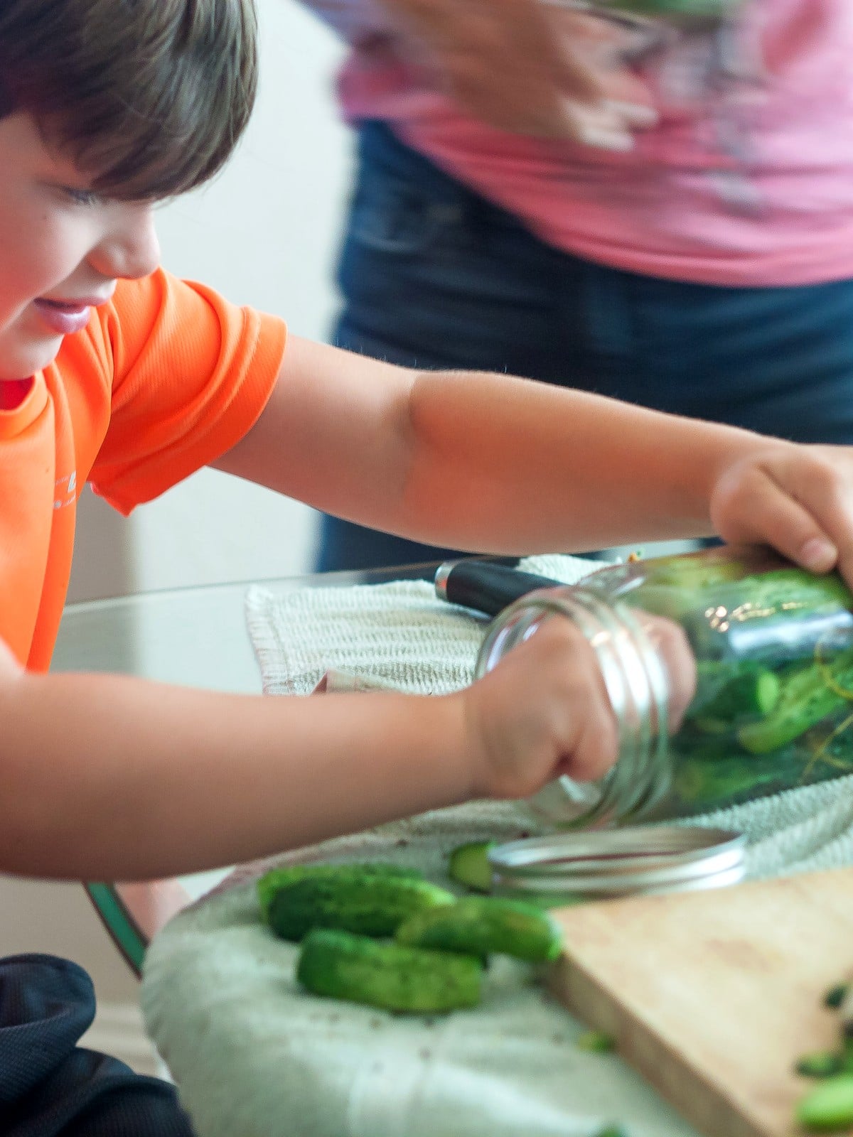 Child helping pack cucumbers into a jar for homemade old-fashioned dill pickles