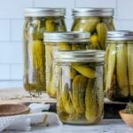 Quart jars of homemade garlic dill pickles with dill and spices on a kitchen counter