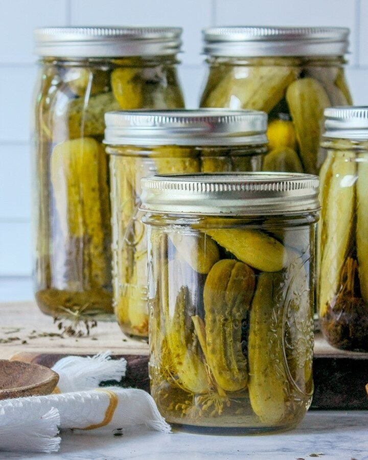 Quart jars of homemade garlic dill pickles with dill and spices on a kitchen counter