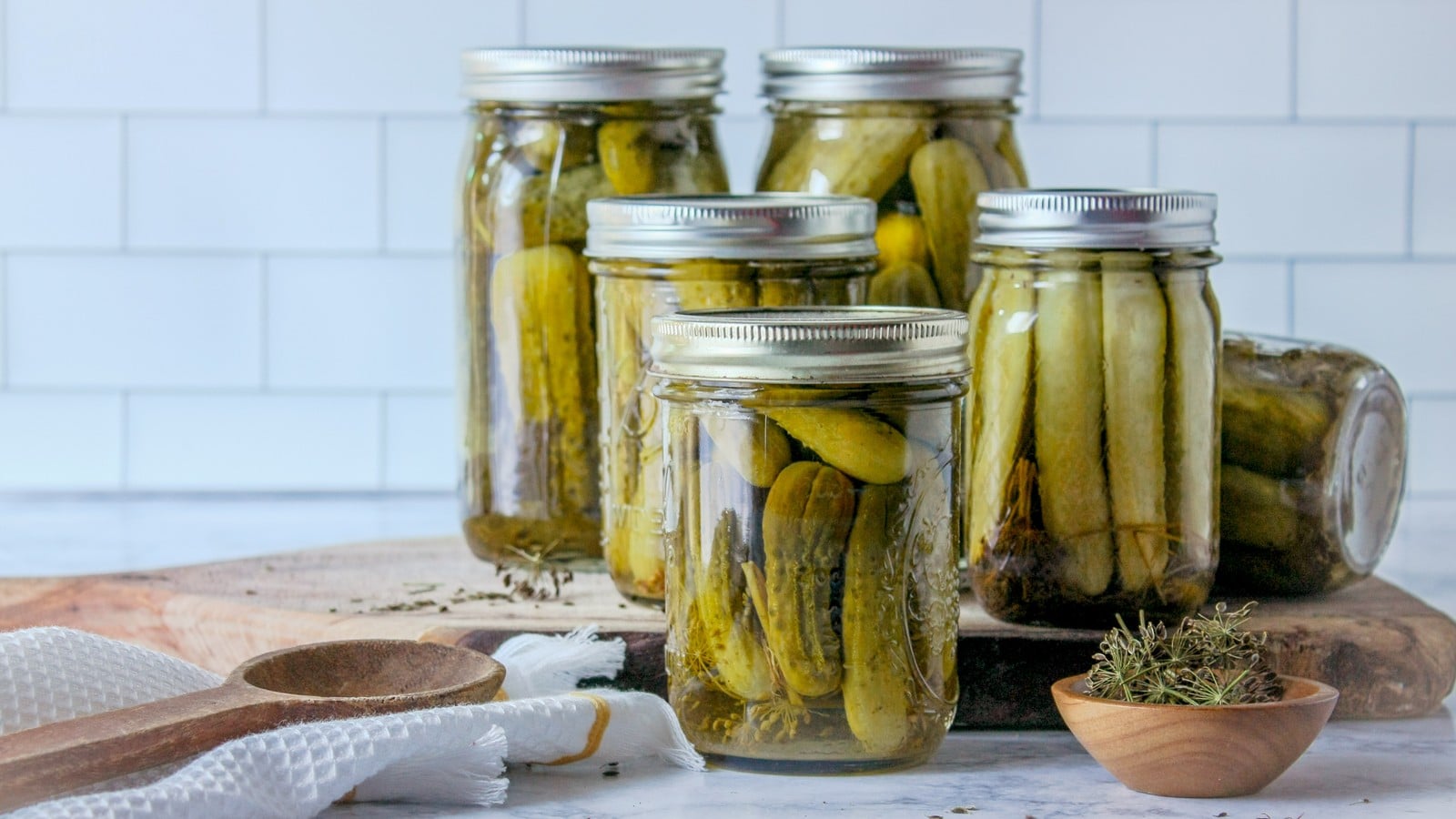 Quart jars of homemade garlic dill pickles with dill and spices on a kitchen counter