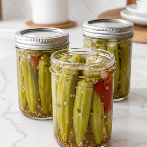 Three jars of Southern pickled okra with whole okra pods, garlic, dill seed, mustard seed, and red pepper.