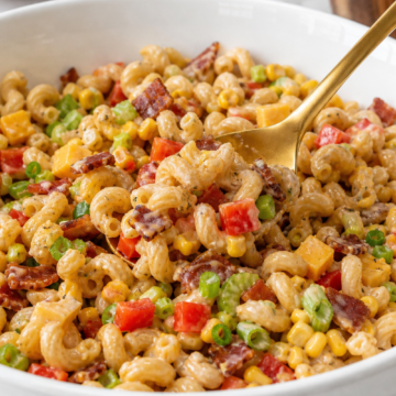 BBQ bacon pasta salad being folded together with cavatappi, bacon, Cheddar, corn, vegetables, and creamy dressing.