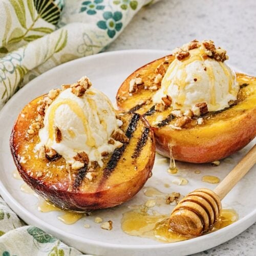 Warm grilled peaches with brown sugar glaze, vanilla ice cream, walnuts, and honey on a white plate.