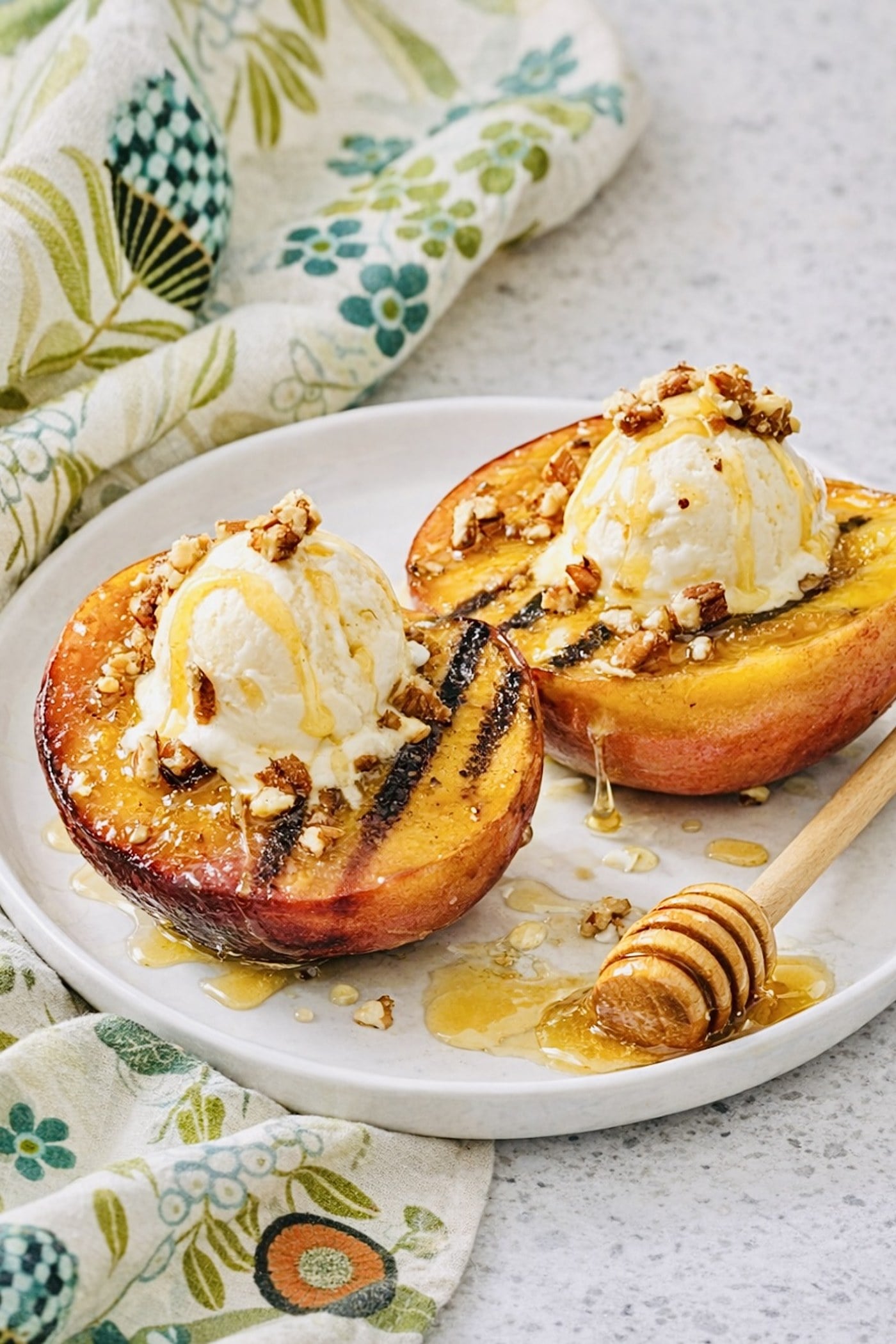 Warm grilled peaches with brown sugar glaze, vanilla ice cream, walnuts, and honey on a white plate.