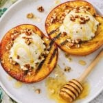 Close-up of grilled peach halves topped with vanilla ice cream, toasted walnuts, and honey.