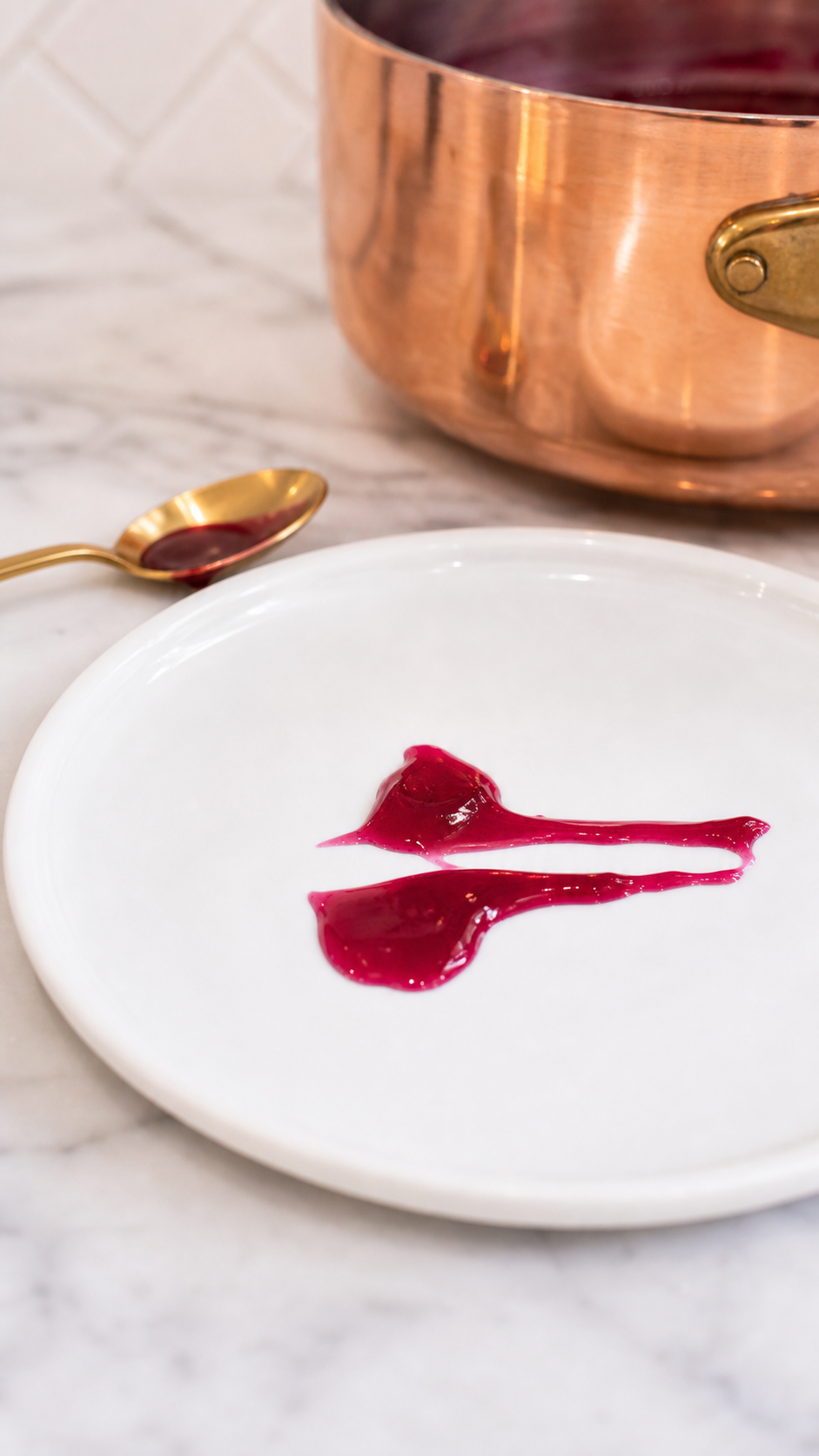 Generated process image of wild Mustang grape jelly plate test streaks beside a brass spoon and copper and brass Mauviel-style cookware.