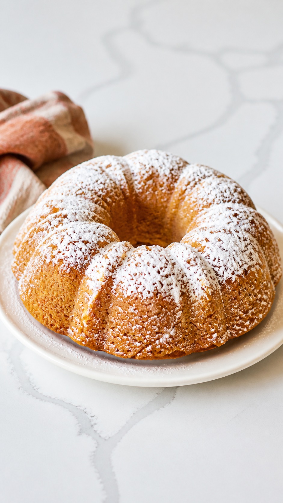 Powdered sugar-dusted 2 ingredient pumpkin Bundt cake on an ivory plate