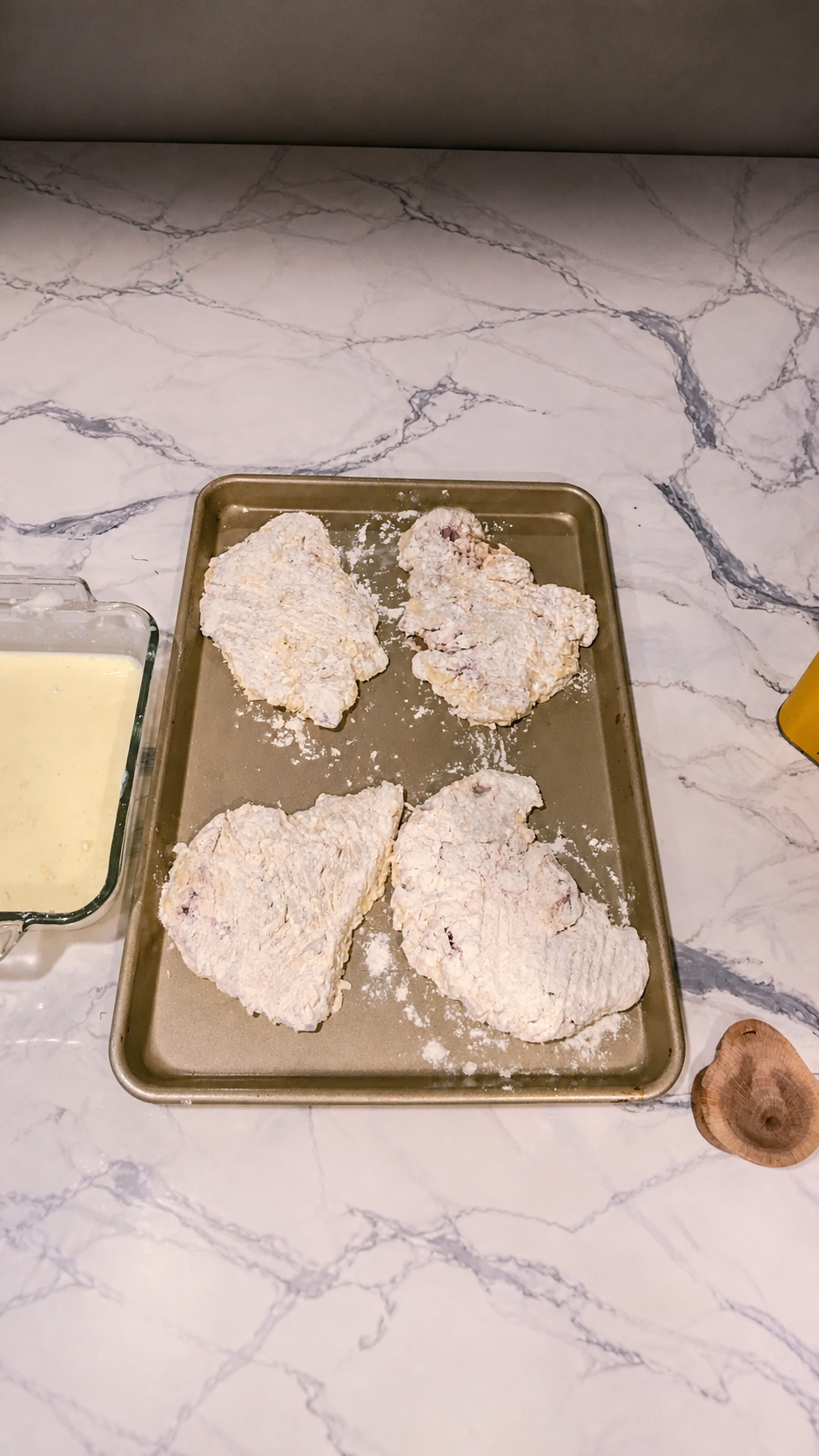 Double-dredged chicken fried steaks resting on a baking sheet before chilling.