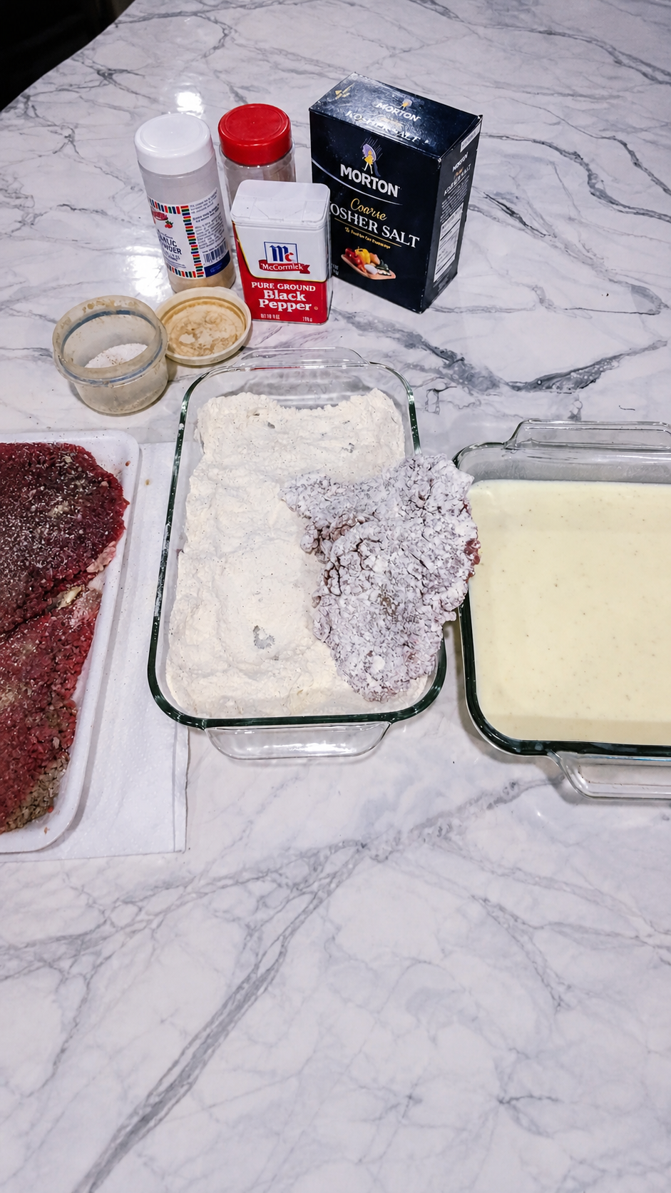 Tenderized steak receiving its first light coating of seasoned flour.