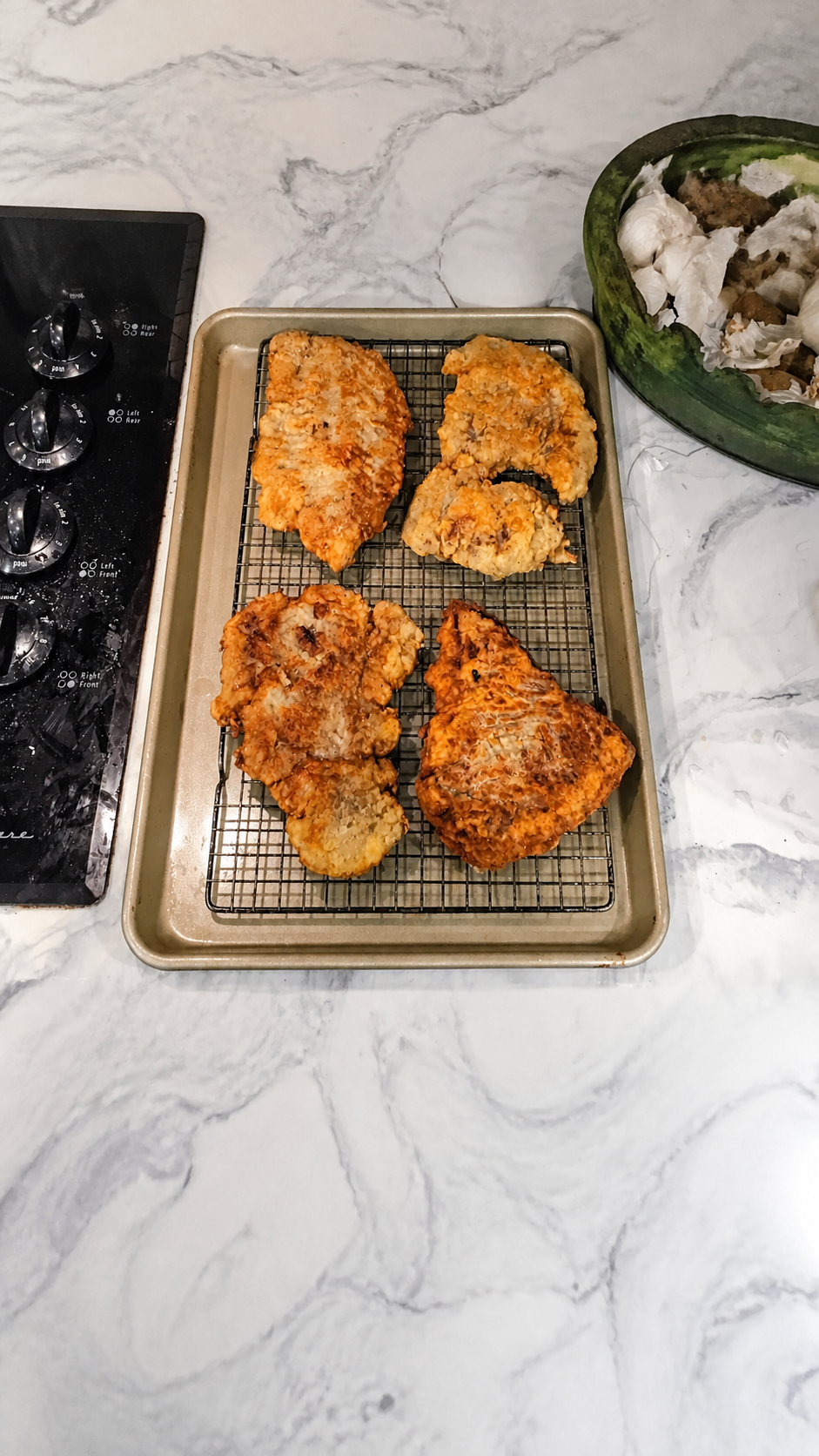 Golden chicken fried steaks draining on a wire rack over a rimmed baking sheet.