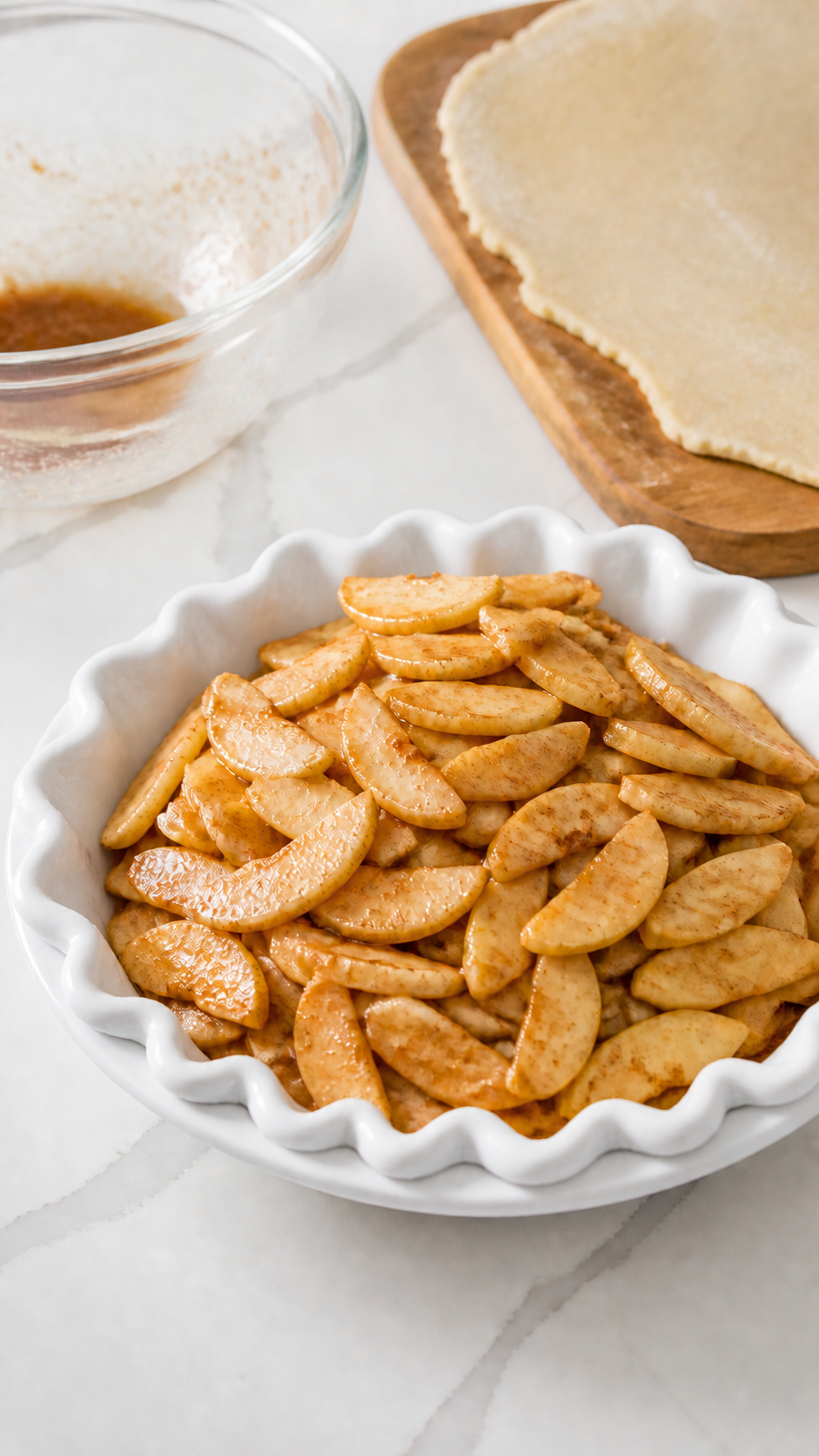 Cinnamon-coated apple slices mounded in a bottom pie crust with liquid left in the bowl.