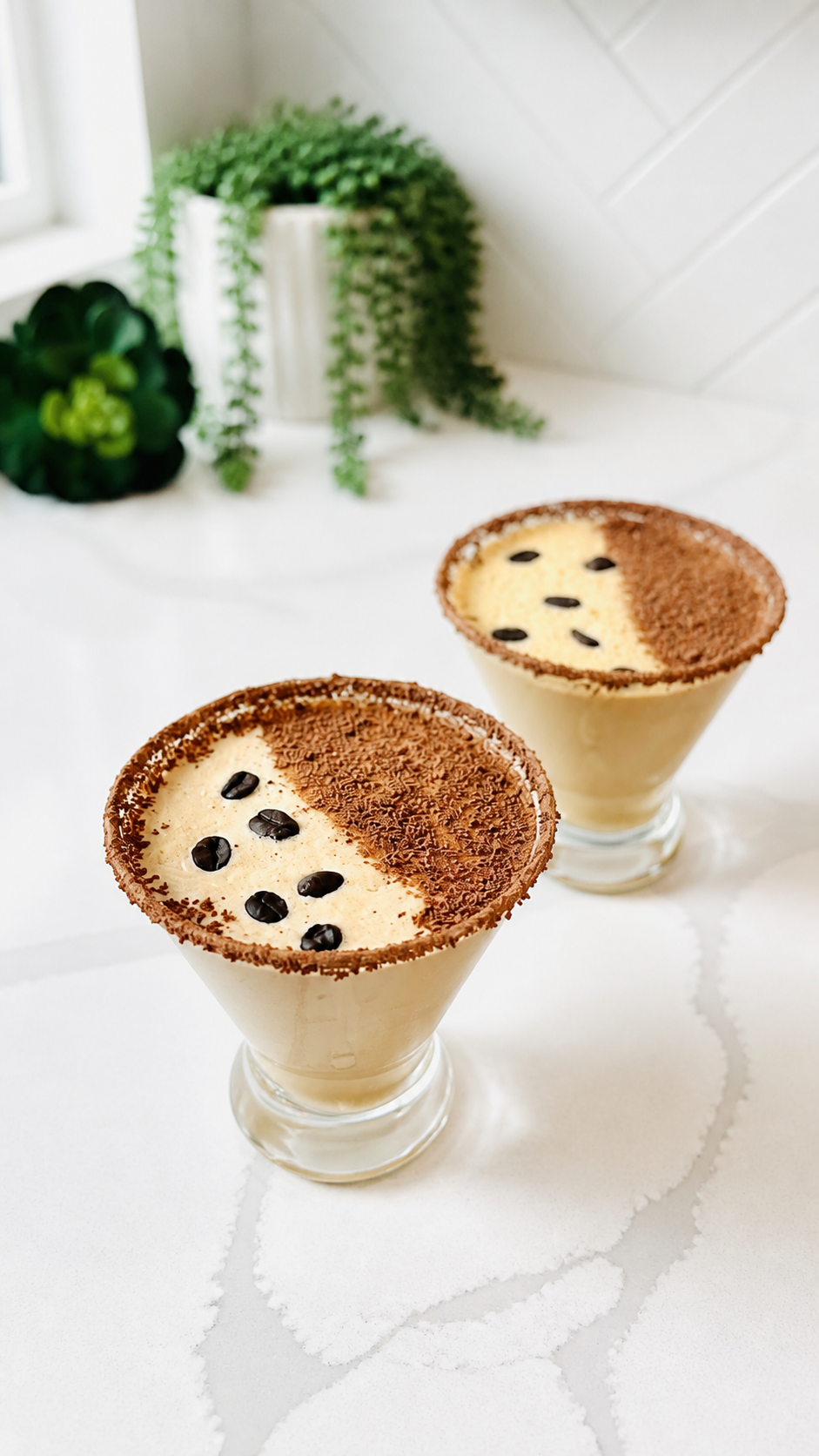 Two finished creamy espresso martinis with chocolate rims and coffee bean garnish.