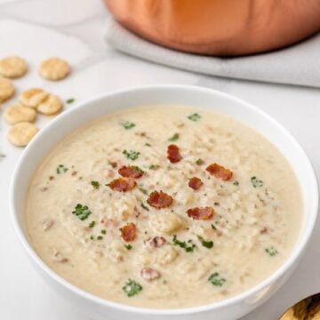 Finished easy New England clam chowder with small pieces of canned clams, peeled potatoes, bacon, and finely chopped parsley beside oyster crackers.
