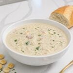 Easy New England clam chowder with small pieces of canned clams, peeled red potatoes, bacon, and finely chopped parsley in a white bowl.