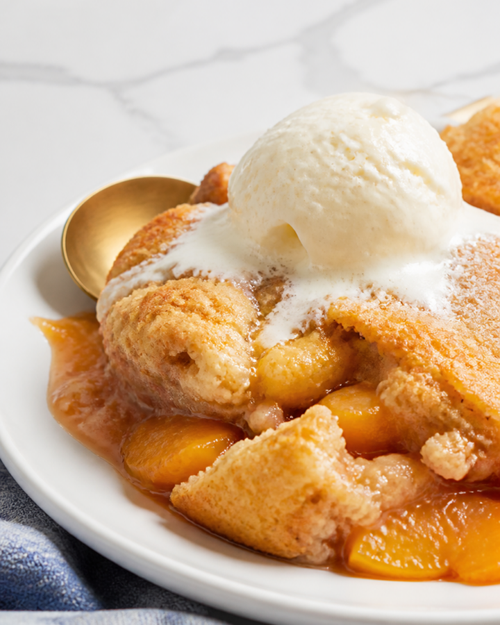 Rustic Bisquick peach cobbler with juicy peaches, golden topping, melting vanilla ice cream, and a plain white plate.